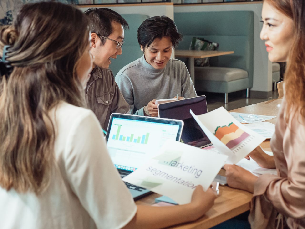 Groupe de collègues échangeant sur des stratégies marketing autour de graphiques et d'ordinateurs portables dans un bureau.